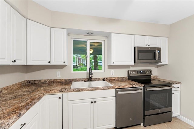 kitchen with dark countertops, a sink, stainless steel appliances, baseboards, and white cabinetry