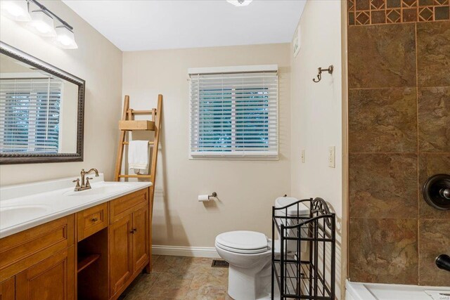 full bathroom with double vanity, a tile shower, a sink, baseboards, and toilet