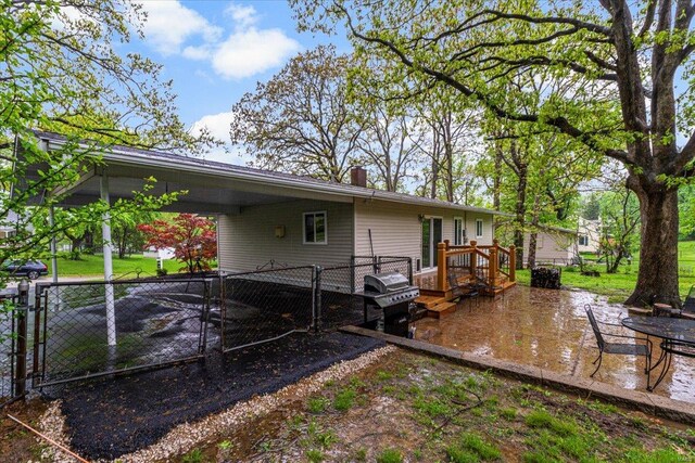 rear view of property featuring a wooden deck, fence, a chimney, an attached carport, and a gate