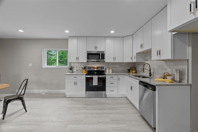 kitchen featuring light stone counters, a sink, appliances with stainless steel finishes, and backsplash
