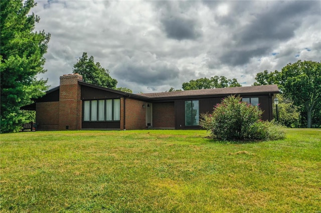 view of front facade featuring brick siding, a chimney, and a front yard