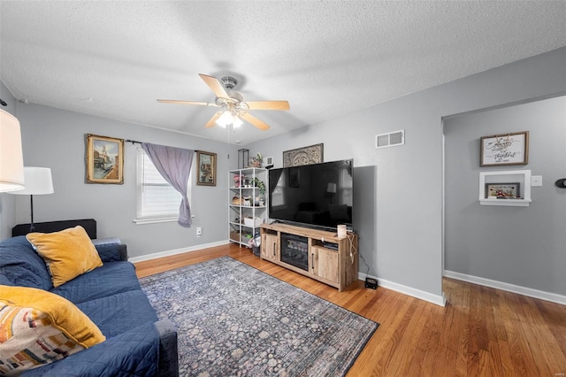 living room featuring visible vents, wood finished floors, baseboards, a textured ceiling, and a ceiling fan