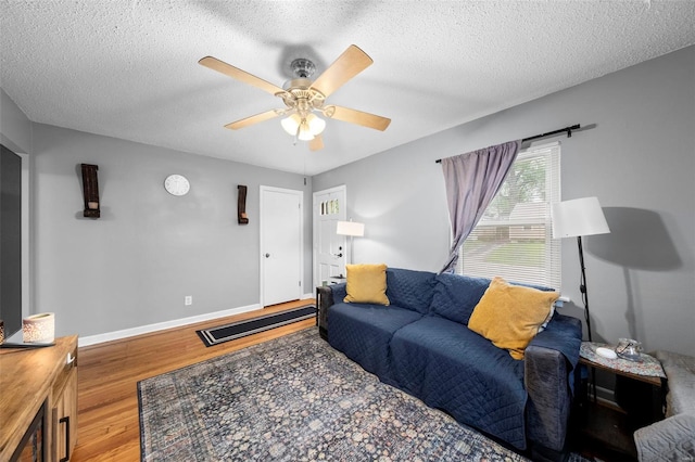 living area featuring a textured ceiling, ceiling fan, baseboards, and wood finished floors