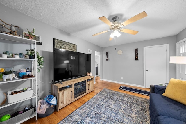 living area with a ceiling fan, a textured ceiling, baseboards, and light wood-style floors