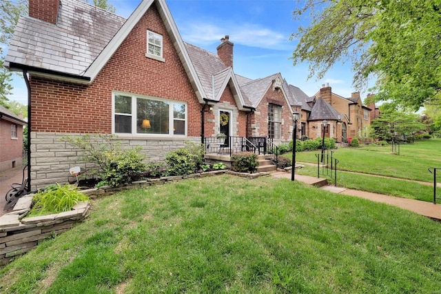 tudor-style house with brick siding, a chimney, a front lawn, and stone siding