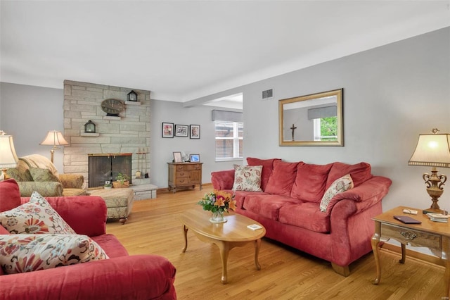 living room featuring a stone fireplace, wood finished floors, and visible vents