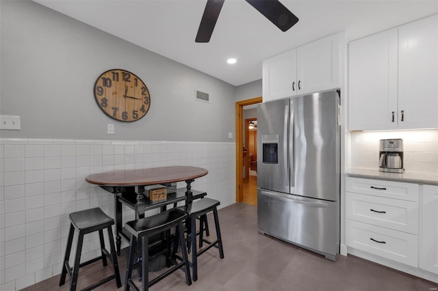 kitchen featuring visible vents, light stone countertops, tile walls, stainless steel fridge, and a ceiling fan