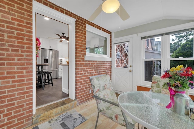 sunroom with a healthy amount of sunlight, brick wall, vaulted ceiling, and wood finished floors