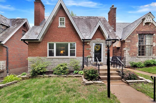 tudor home with brick siding, a front yard, a chimney, and stone siding