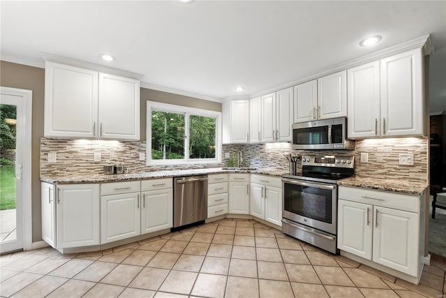 kitchen with stainless steel appliances, tasteful backsplash, white cabinets, light tile patterned flooring, and ornamental molding