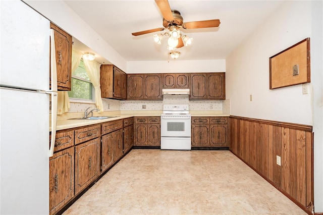 kitchen featuring a sink, a wainscoted wall, under cabinet range hood, light floors, and white appliances