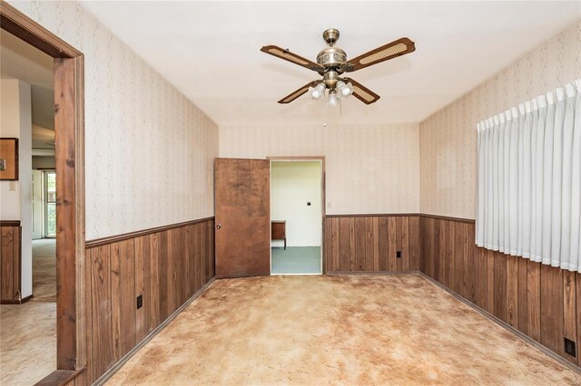 spare room featuring wooden walls, wallpapered walls, ceiling fan, and wainscoting