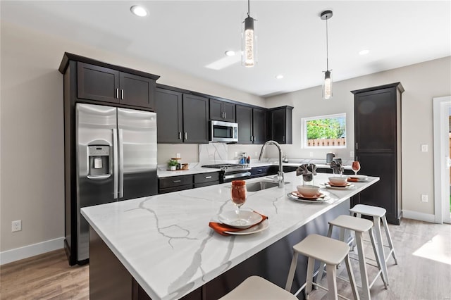 kitchen with light wood-style flooring, a sink, appliances with stainless steel finishes, baseboards, and light stone countertops