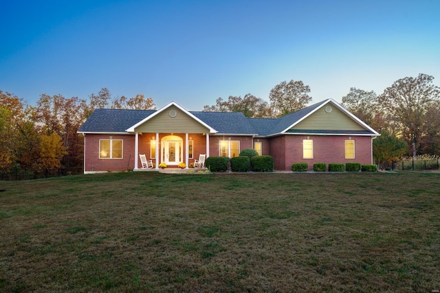view of front of property featuring a porch, a yard, and brick siding