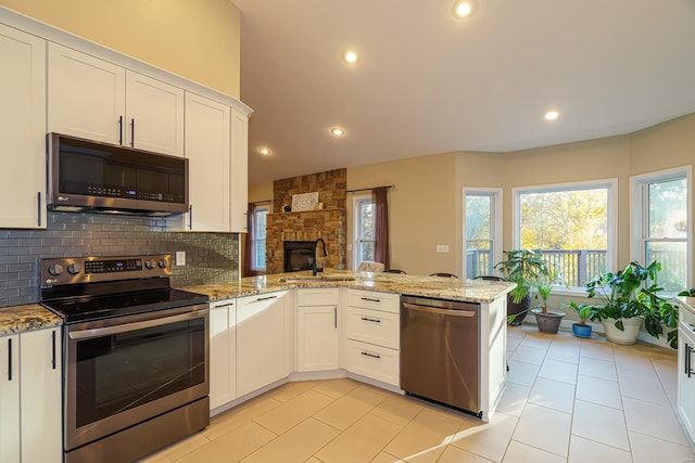 kitchen with a sink, light stone counters, a peninsula, white cabinetry, and appliances with stainless steel finishes