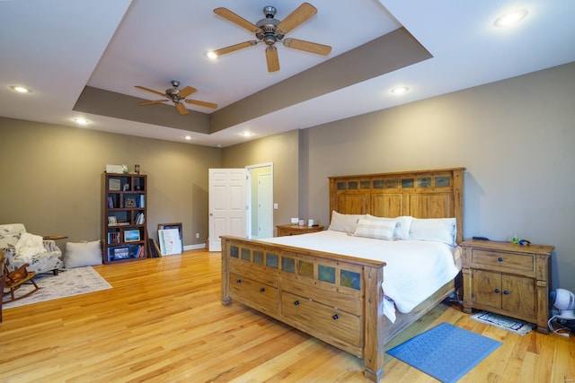 bedroom with ceiling fan, a tray ceiling, baseboards, recessed lighting, and wood finished floors
