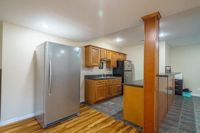 kitchen featuring brown cabinetry, a sink, dark wood-style flooring, and freestanding refrigerator