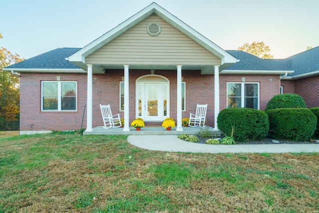 view of front facade featuring a porch, a front lawn, roof with shingles, and brick siding