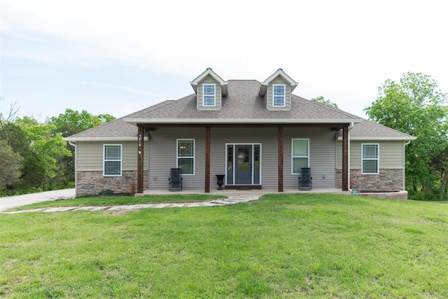 view of front facade with a shingled roof, a front yard, and stone siding