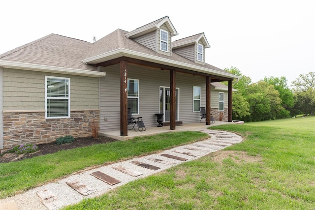 view of front of property featuring a patio, a shingled roof, stone siding, and a front lawn