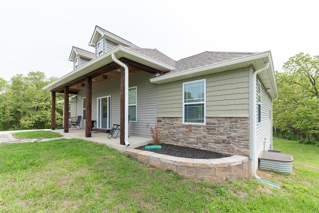 view of front facade featuring a shingled roof, a front yard, a patio area, and stone siding