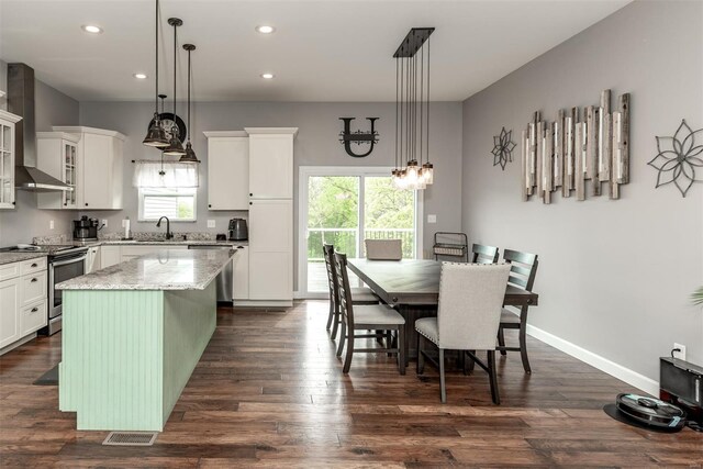kitchen featuring a kitchen island, wall chimney exhaust hood, white cabinetry, a sink, and stainless steel appliances