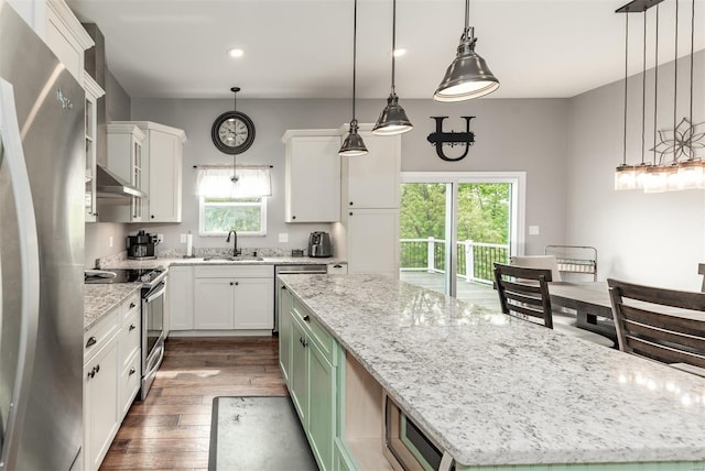 kitchen with dark wood-style flooring, wall chimney range hood, a center island, a sink, and appliances with stainless steel finishes