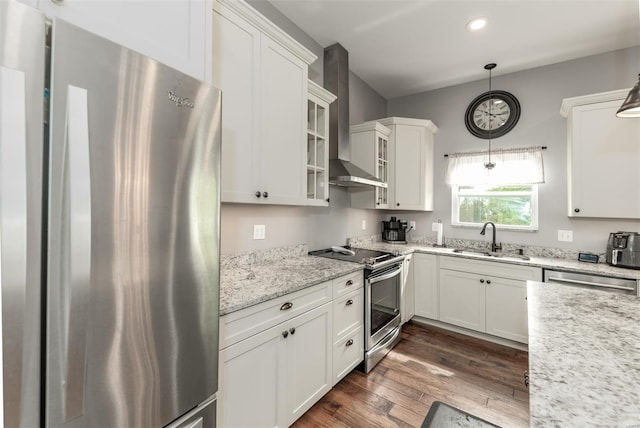 kitchen with wall chimney range hood, appliances with stainless steel finishes, dark wood finished floors, a sink, and white cabinets