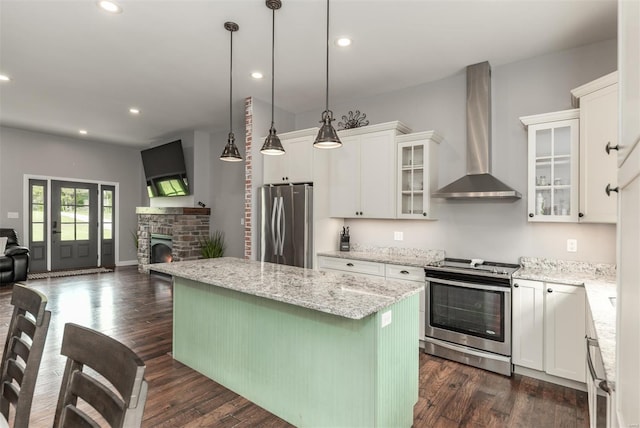kitchen featuring open floor plan, wall chimney range hood, a center island, white cabinets, and appliances with stainless steel finishes