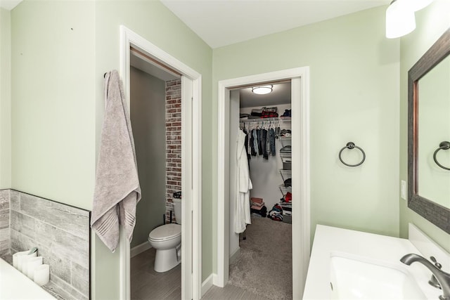 bathroom featuring a walk in closet, baseboards, vanity, and toilet