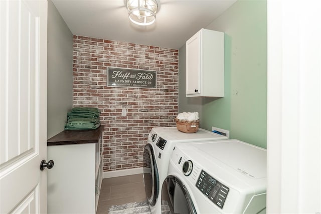 clothes washing area featuring brick wall, cabinet space, and independent washer and dryer