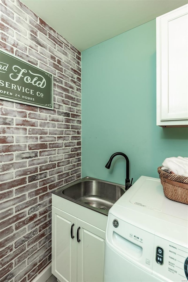 clothes washing area with washer / dryer, brick wall, cabinet space, and a sink