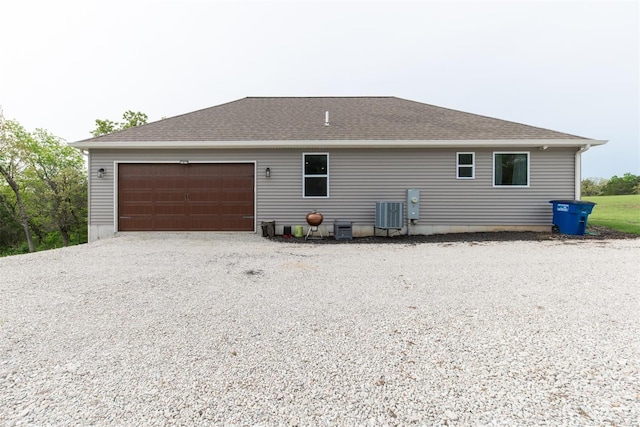 back of property with an attached garage, a shingled roof, central air condition unit, and driveway