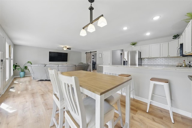 dining space with recessed lighting, a ceiling fan, light wood finished floors, and a barn door