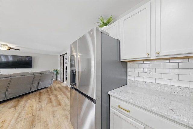 kitchen with decorative backsplash, light stone countertops, stainless steel fridge with ice dispenser, light wood-style floors, and white cabinetry
