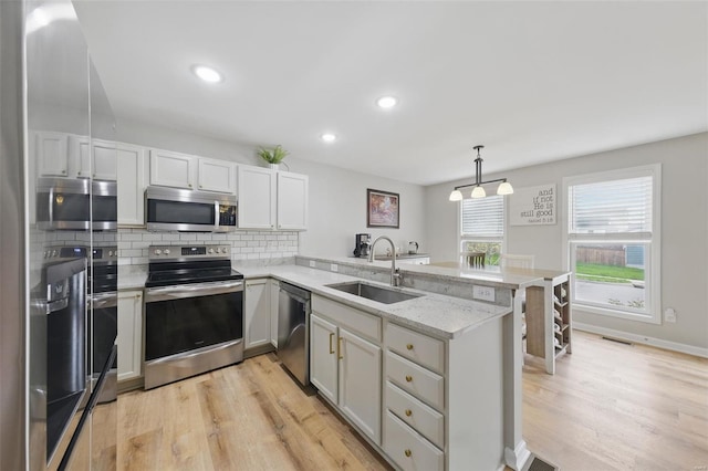 kitchen with a sink, light wood-style flooring, a peninsula, and stainless steel appliances