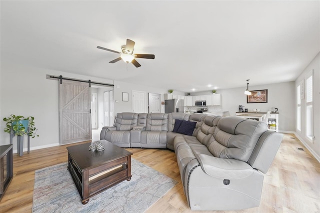 living area with ceiling fan, a barn door, baseboards, and light wood finished floors