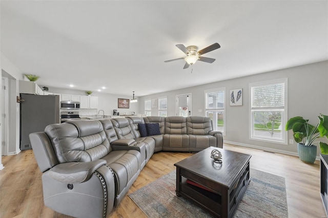living room featuring a ceiling fan, visible vents, baseboards, light wood finished floors, and recessed lighting