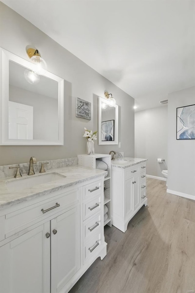 bathroom with baseboards, two vanities, a sink, and wood finished floors