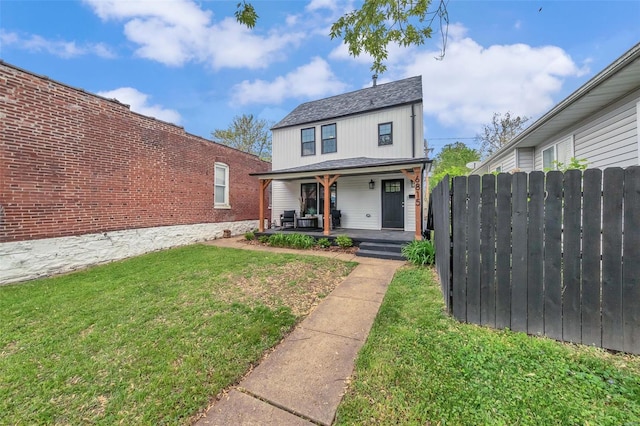 traditional-style house featuring a front yard, covered porch, and fence