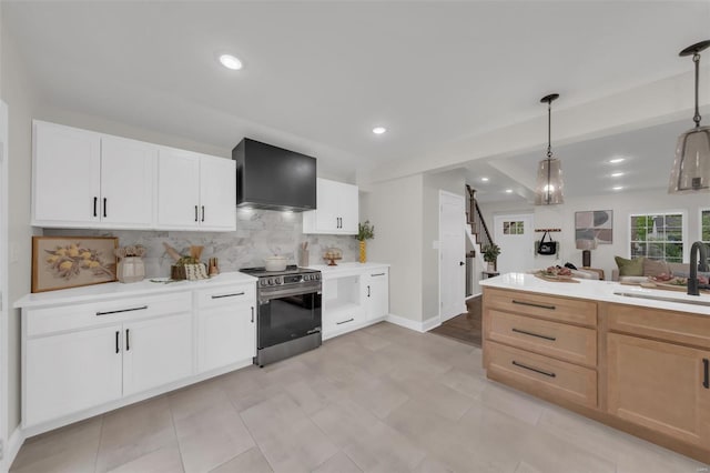 kitchen with decorative backsplash, stainless steel range with electric stovetop, light countertops, a sink, and wall chimney exhaust hood