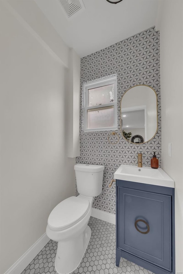 half bath featuring vanity, toilet, visible vents, baseboards, and wallpapered walls