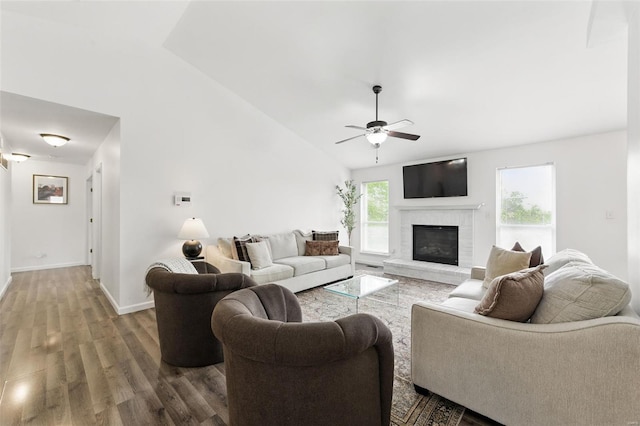living area with a brick fireplace, a ceiling fan, baseboards, wood finished floors, and vaulted ceiling