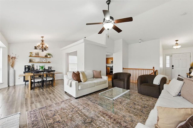 living room with ceiling fan with notable chandelier, plenty of natural light, vaulted ceiling, and light wood-type flooring