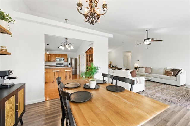 dining space featuring ceiling fan with notable chandelier, baseboards, vaulted ceiling, and wood finished floors