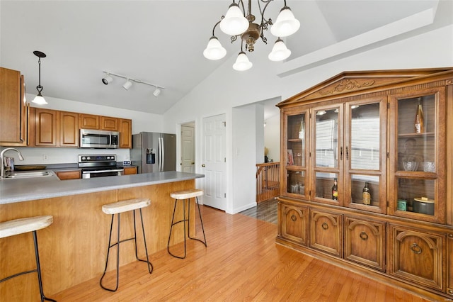 kitchen featuring brown cabinets, a sink, stainless steel appliances, a peninsula, and a kitchen bar