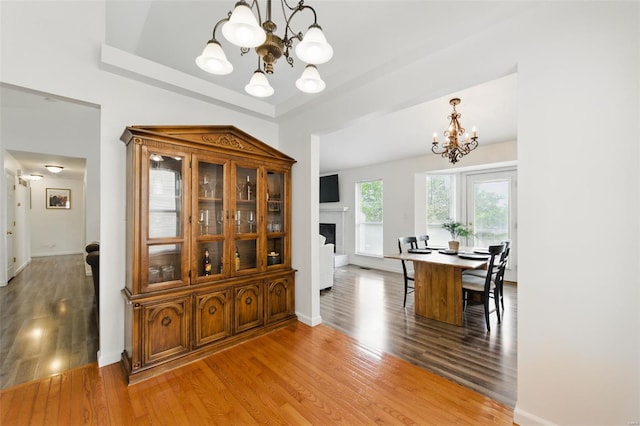 dining area with a raised ceiling, a fireplace, light wood-style flooring, and a notable chandelier