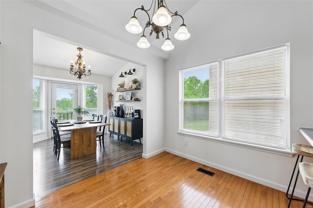 dining room featuring a notable chandelier, light wood-style floors, baseboards, lofted ceiling, and visible vents