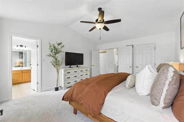 bedroom with ceiling fan, light colored carpet, two closets, ensuite bathroom, and vaulted ceiling