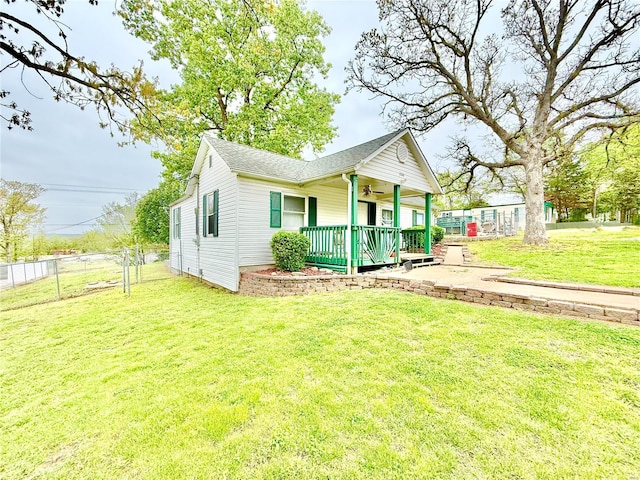 view of front of home with a shingled roof, covered porch, ceiling fan, fence, and a front lawn